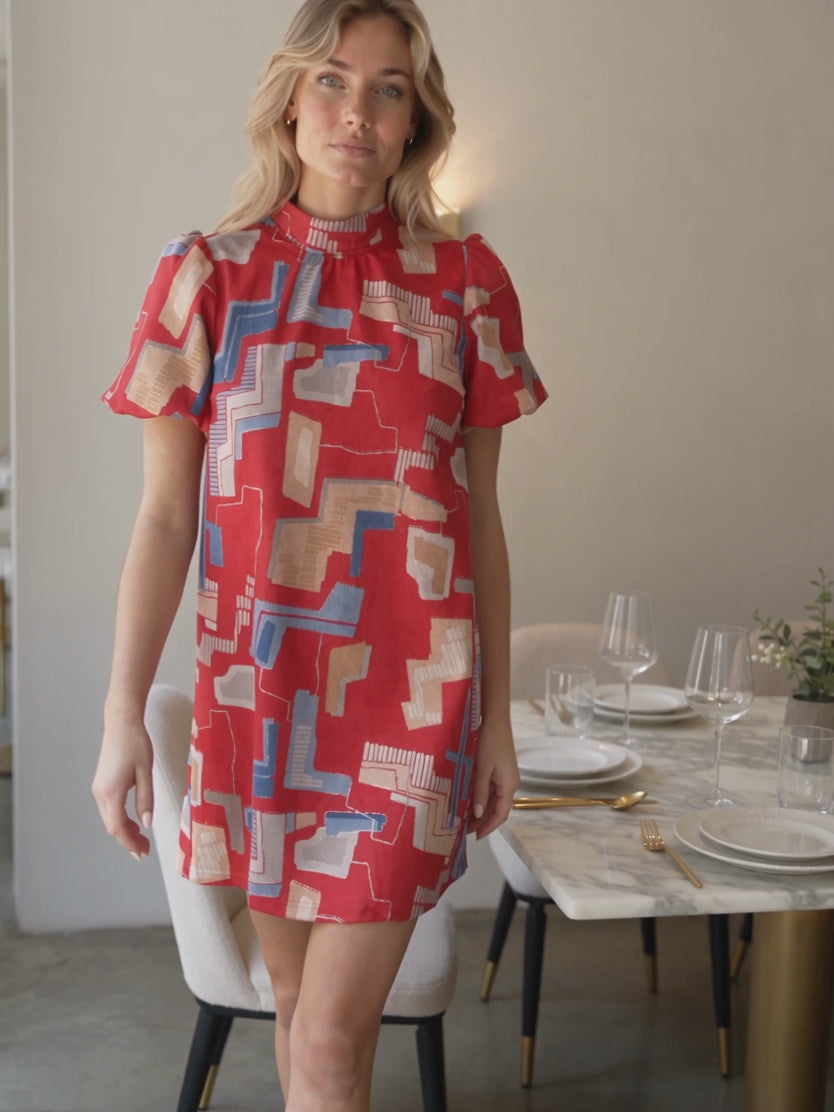 Elsa walking in the red geometric mini dress to show its sleeve and shift-body movement.