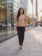 The latte split neck faux leather top worn by Shweta at a city street, stepping forward and turning to show the side and the fit.