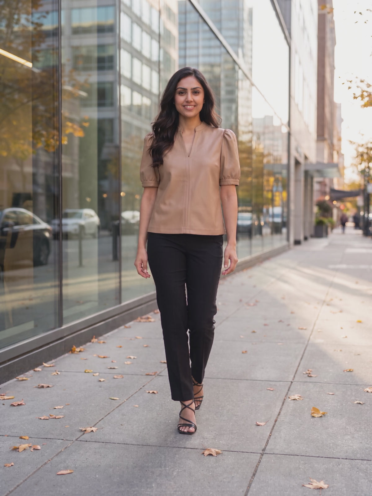 The latte split neck faux leather top worn by Shweta at a city street, stepping forward and turning to show the side and the fit.