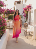 The hibiscus ombre one shoulder pleated maxi dress worn by Shweta at a sunlit villa terrace at golden hour, stepping forward and turning to show the side and the fit.
