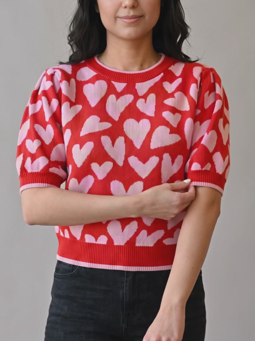 Shweta smooths the cuff and turns to show the Small heart sweater's sleeve structure and drape.