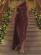 The metallic burgundy pleated one shoulder maxi dress worn on a candlelit holiday staircase, stepping down and turning to show the pleats and the waist cutout.