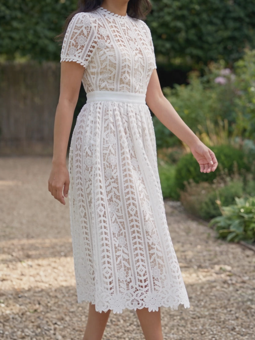 Shweta walking in the Sunset Stroll white lace midi dress, showing structured skirt movement.