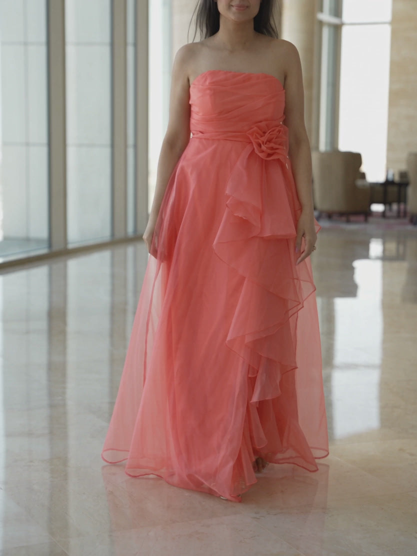 Coral organza maxi dress moving through an evening lounge as its layered ruffles and trailing hem flow.