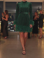 The green velvet feather trim mini dress worn at a holiday party, walking so the feathers at the hem and cuffs move.