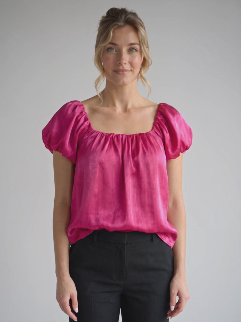 Elsa gently moves in the Magenta puff sleeve satin top to show its drape and sleeve volume.