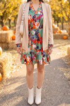 Green abstract print ruffle hem dress styled for a fall pumpkin patch with a camel cardigan blazer, cream western booties and a cream chain shoulder bag.