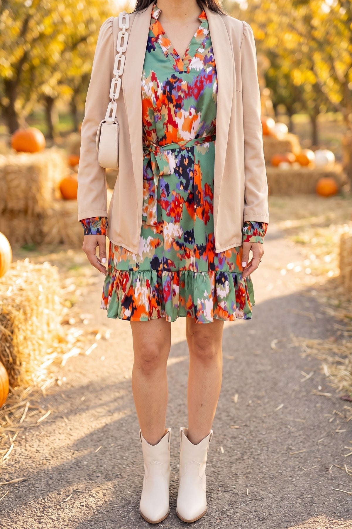 Green abstract print ruffle hem dress styled for a fall pumpkin patch with a camel cardigan blazer, cream western booties and a cream chain shoulder bag.
