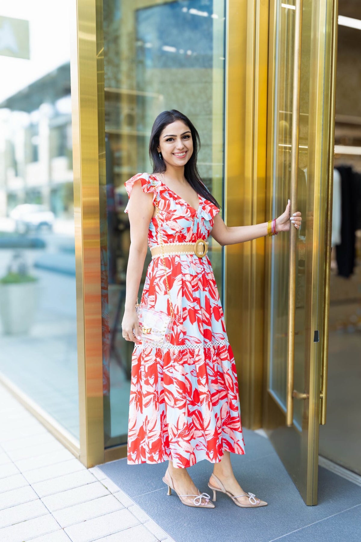 Shweta Sobat in a red and white floral midi dress, holding open a gold door