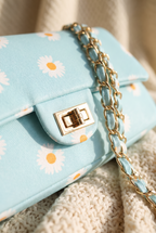 Close-up of the Vera bag gold twist lock, daisy print flap and fabric-woven chain