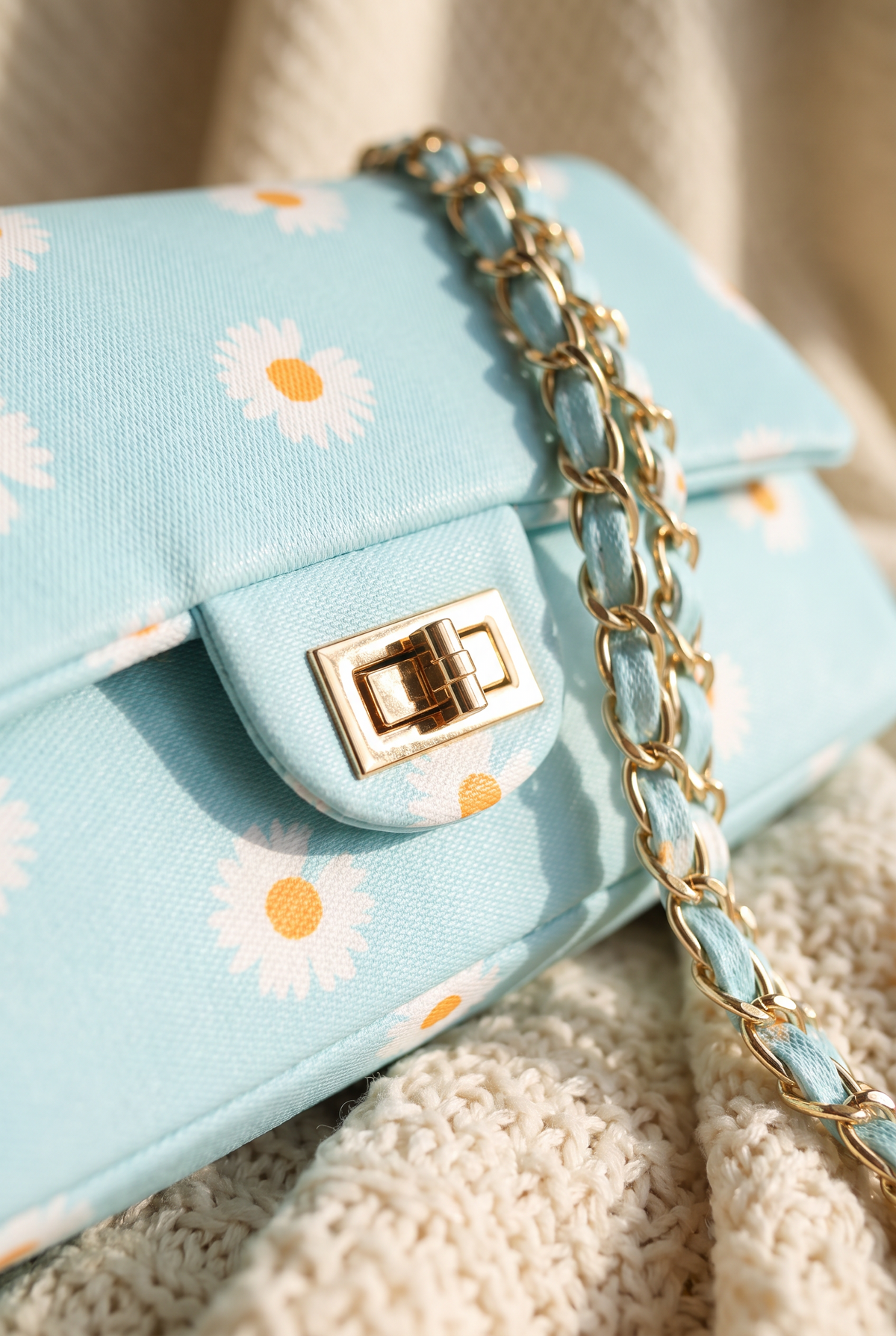 Close-up of the Vera bag gold twist lock, daisy print flap and fabric-woven chain