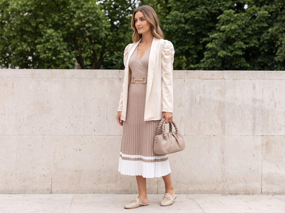 Woman in a beige blazer over a pleated sweater midi dress with a nude braided-handle bag and beige flat mules