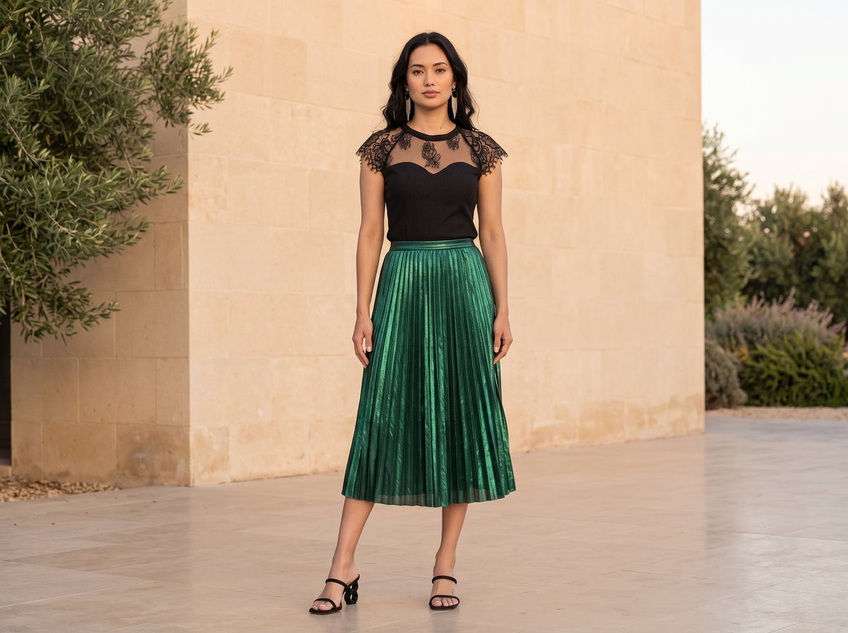 Woman in a black lace ruffle-sleeve top with a green metallic pleated skirt, black heeled sandals and silver earrings