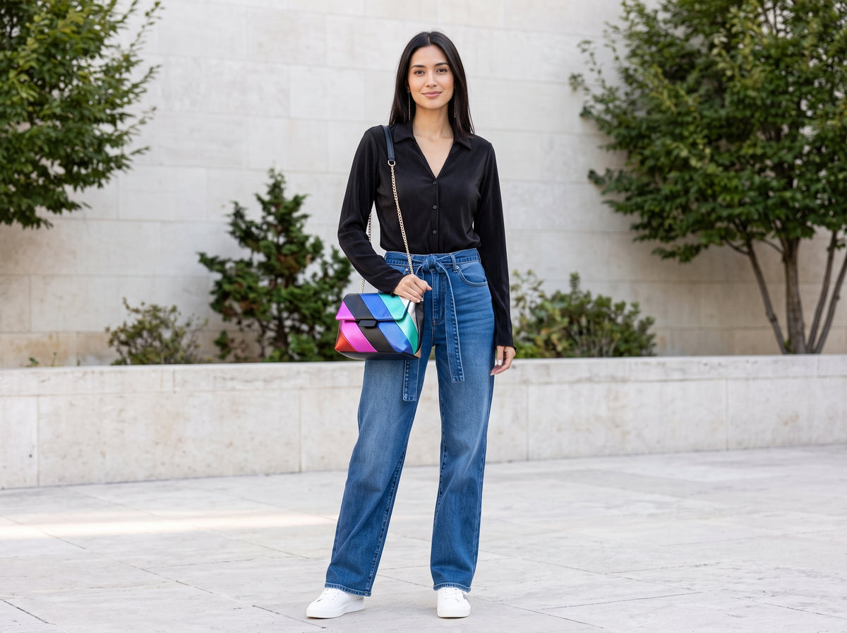 Woman in a black long-sleeve top, belted wide-leg jeans and white sneakers with a multicolour striped crossbody bag