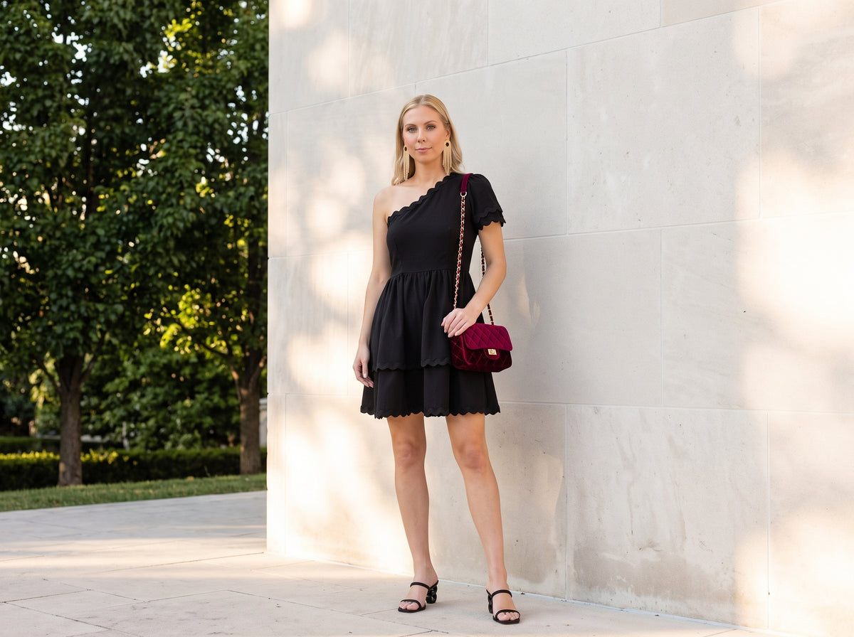 Woman in a black one-shoulder mini dress and heeled slide sandals with a burgundy quilted velvet crossbody purse