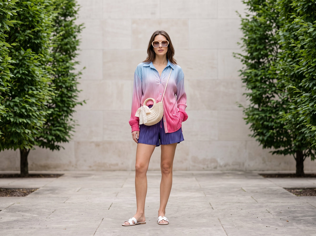 Woman in a blue-to-pink ombre shirt and shorts set with white slides, a rattan crossbody and sunglasses