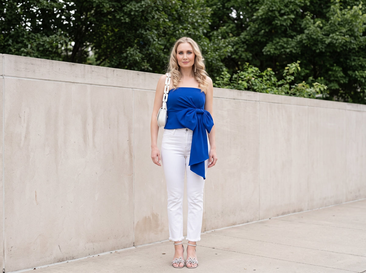 Woman in a cobalt blue side-bow tube top with white cropped jeans, silver sandals and a white chain bag