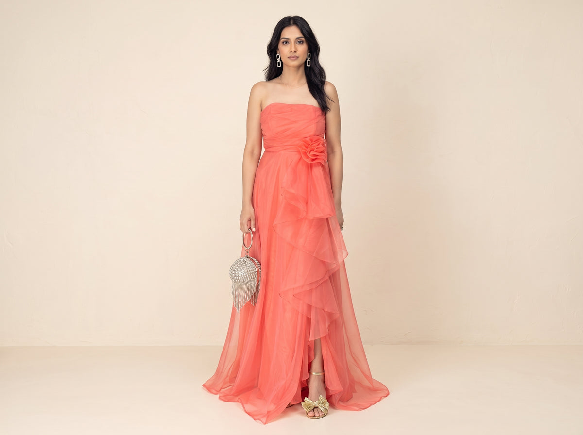 Woman in a coral organza maxi gown with gold bow ankle-strap sandals, a crystal fringe clutch and rhinestone drop earrings