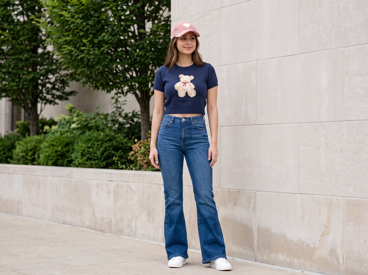 Woman in a cropped teddy bear sweater with flare jeans, white sneakers and a pink heart cap