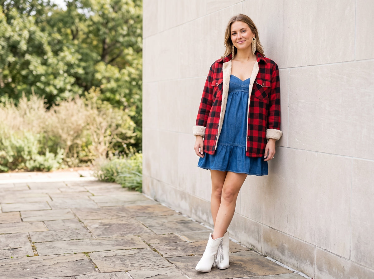 Woman in a denim babydoll dress and plaid sherpa-lined jacket with gold fringe earrings and white rhinestone fringe western booties