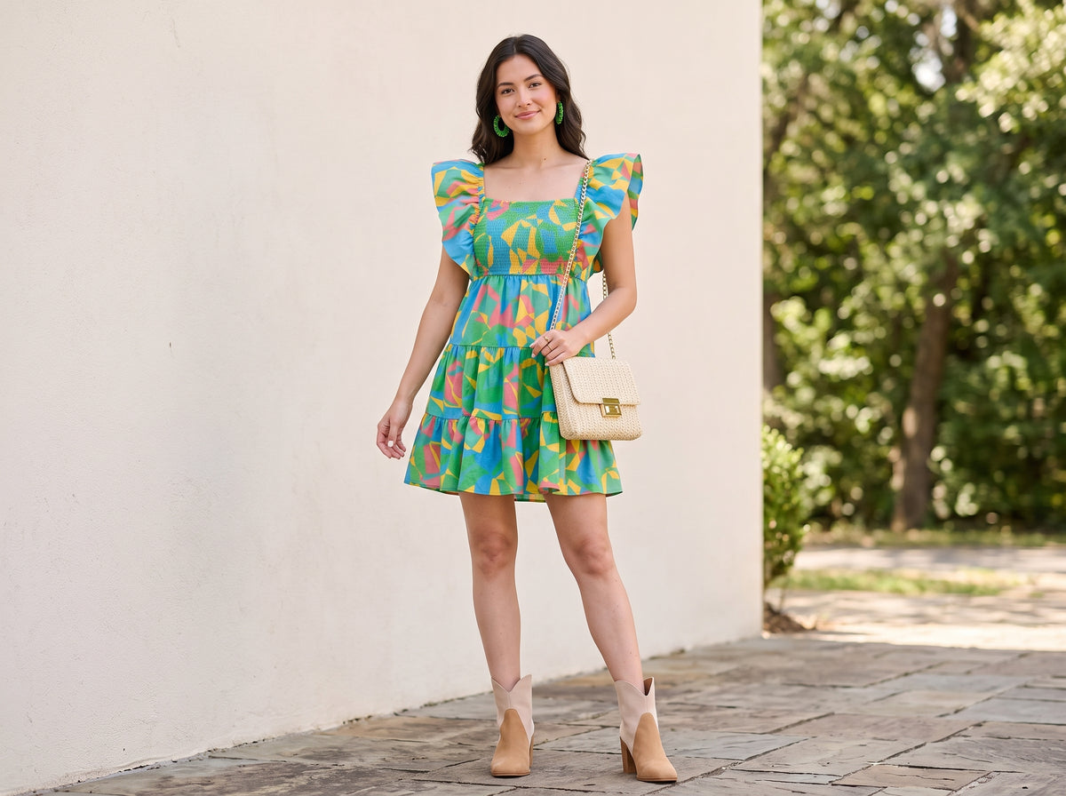 Woman in a geometric print flutter-sleeve mini dress with suede ankle booties, a braided chain crossbody and woven hoop earrings