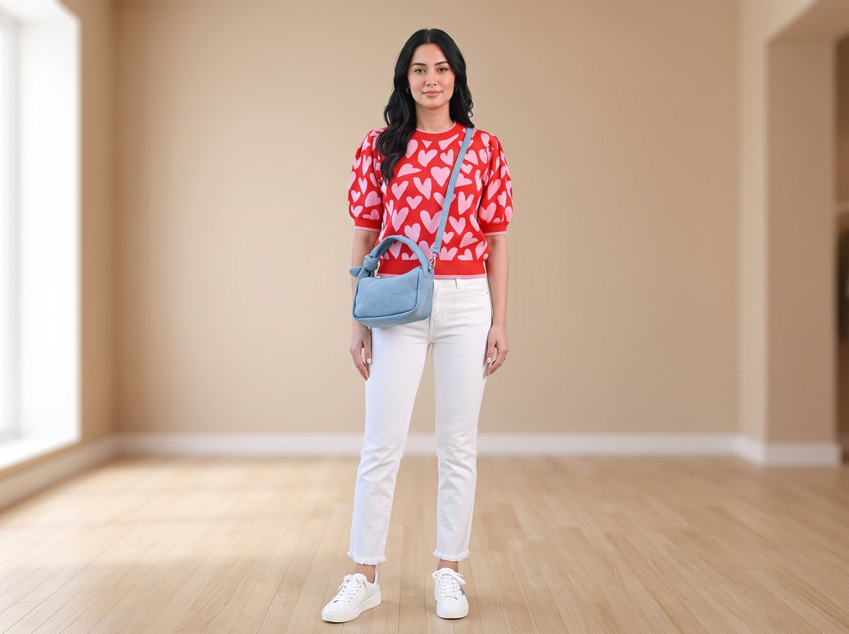 Woman in a heart-print puff-sleeve sweater and white jeans with a light denim crossbody bag and white sneakers
