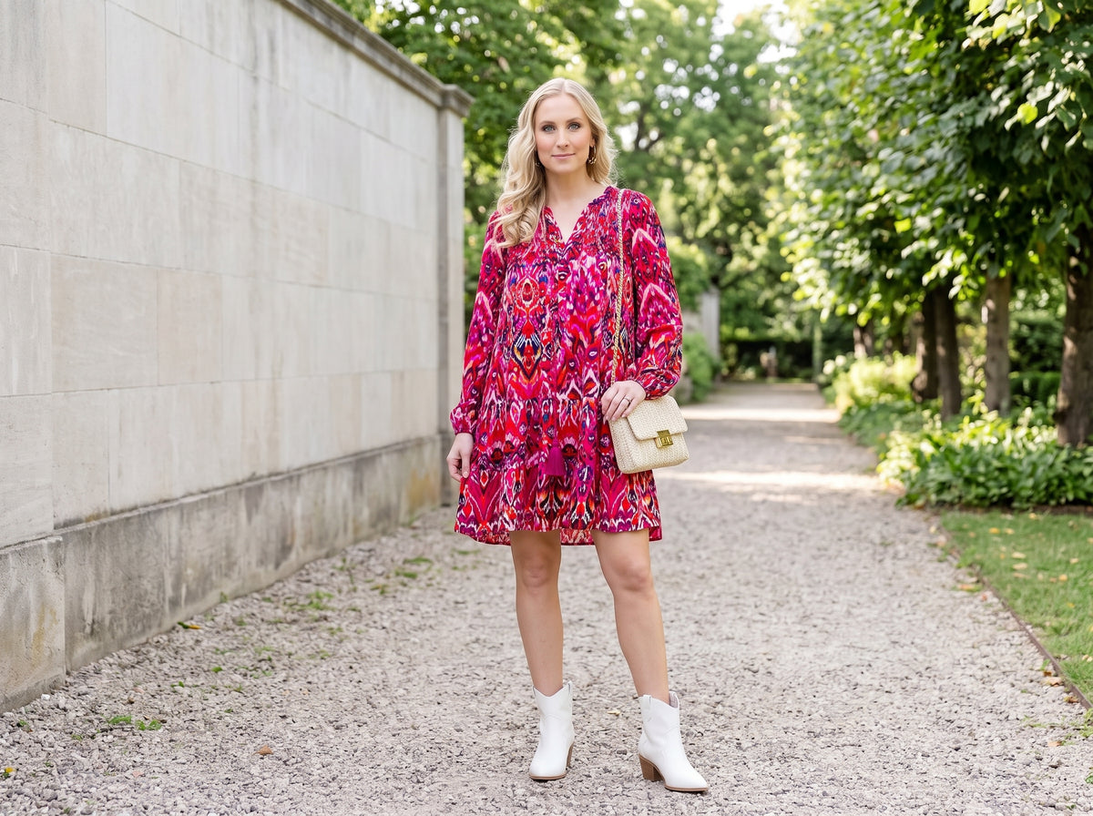 Woman in a magenta print tiered short dress with white western booties, a braided chain crossbody and gold bow hoop earrings
