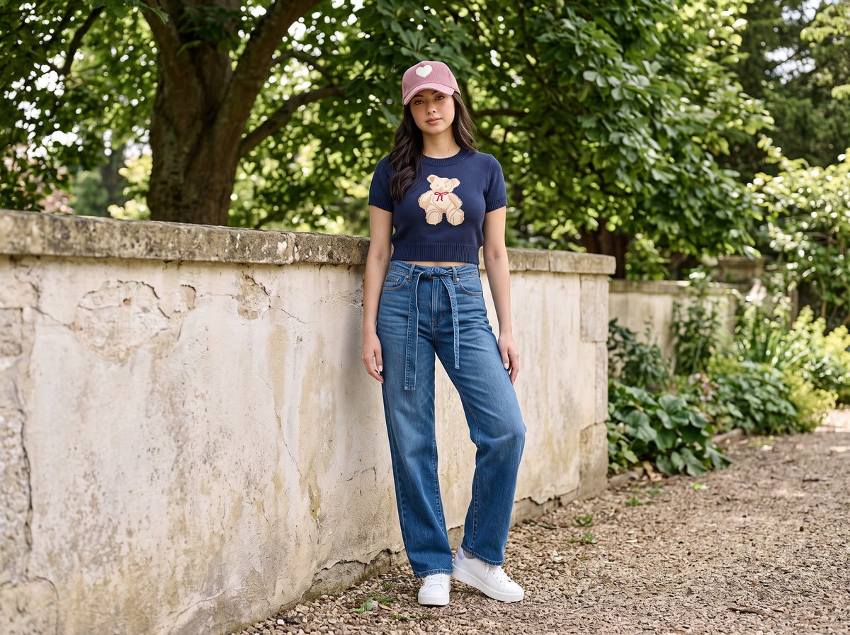 Woman in a mauve corduroy heart cap, navy teddy bear cropped sweater and belted wide-leg jeans
