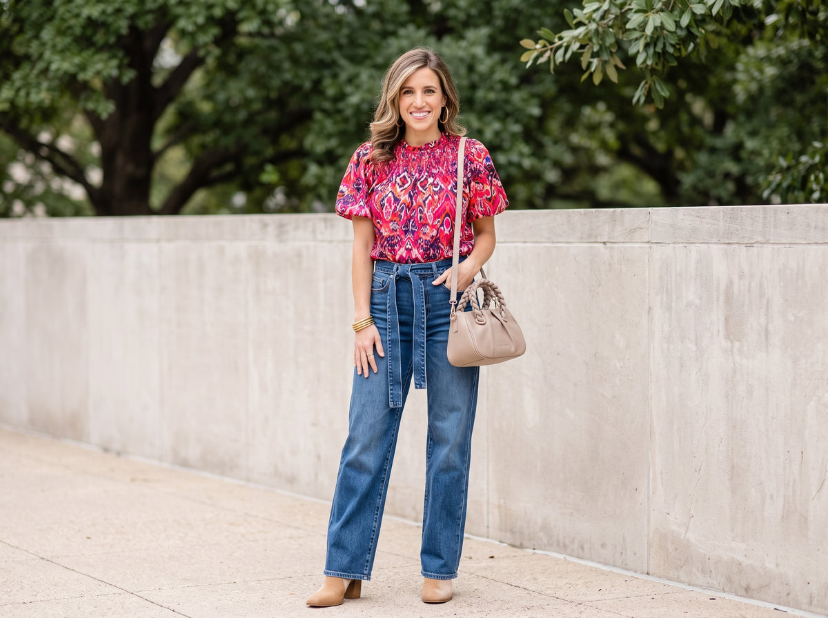 Woman in a pink floral puff-sleeve top with wide-leg jeans, suede ankle booties and a nude crossbody