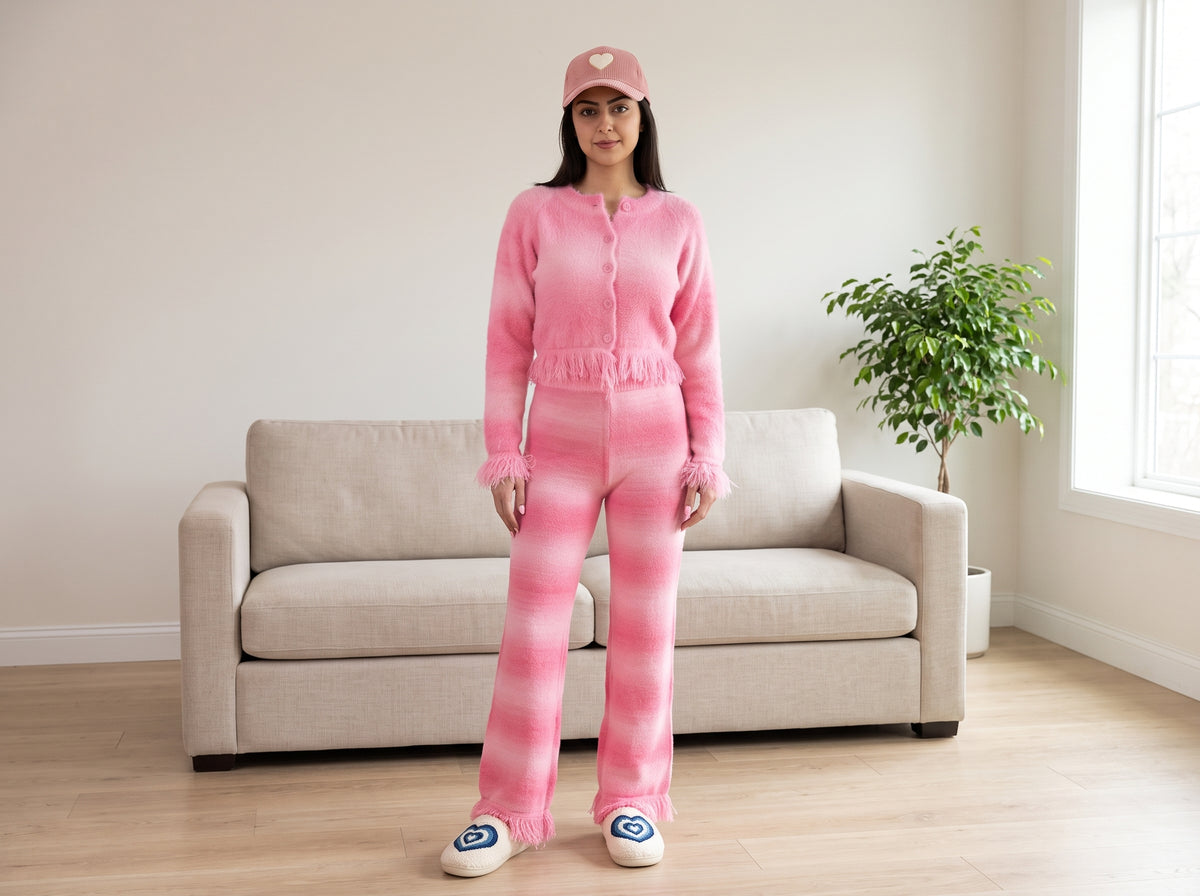 Woman in a pink fuzzy cardigan top with matching lounge pants, heart slippers and a pink cap