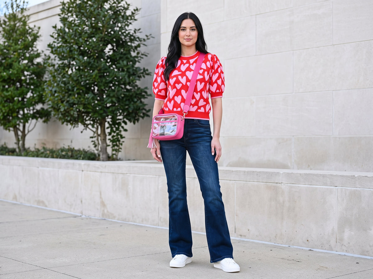 Woman in a pink heart-pattern sweater and flare jeans with a clear pink tassel crossbody bag and white glitter-star sneakers