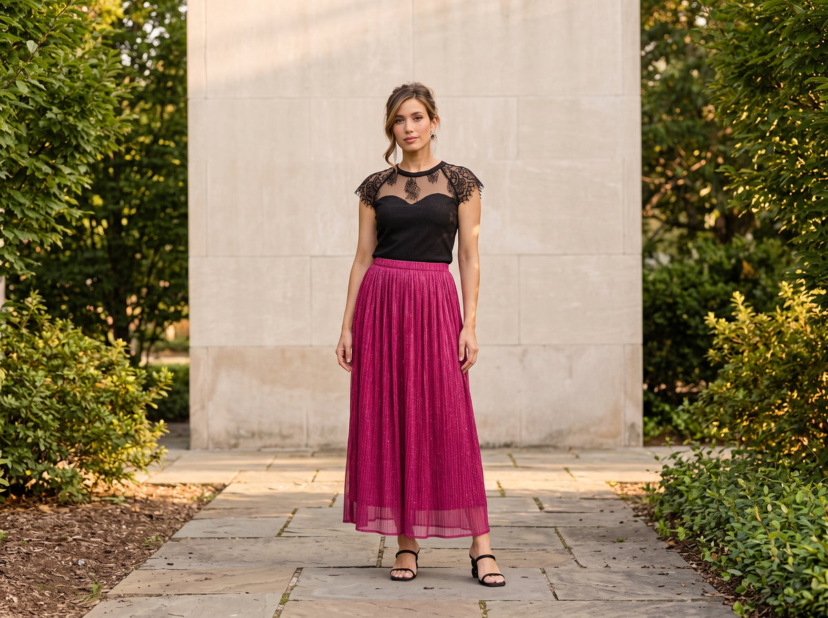 Woman in a pink sparkle pleated maxi skirt with a black lace top, black heeled sandals and silver earrings
