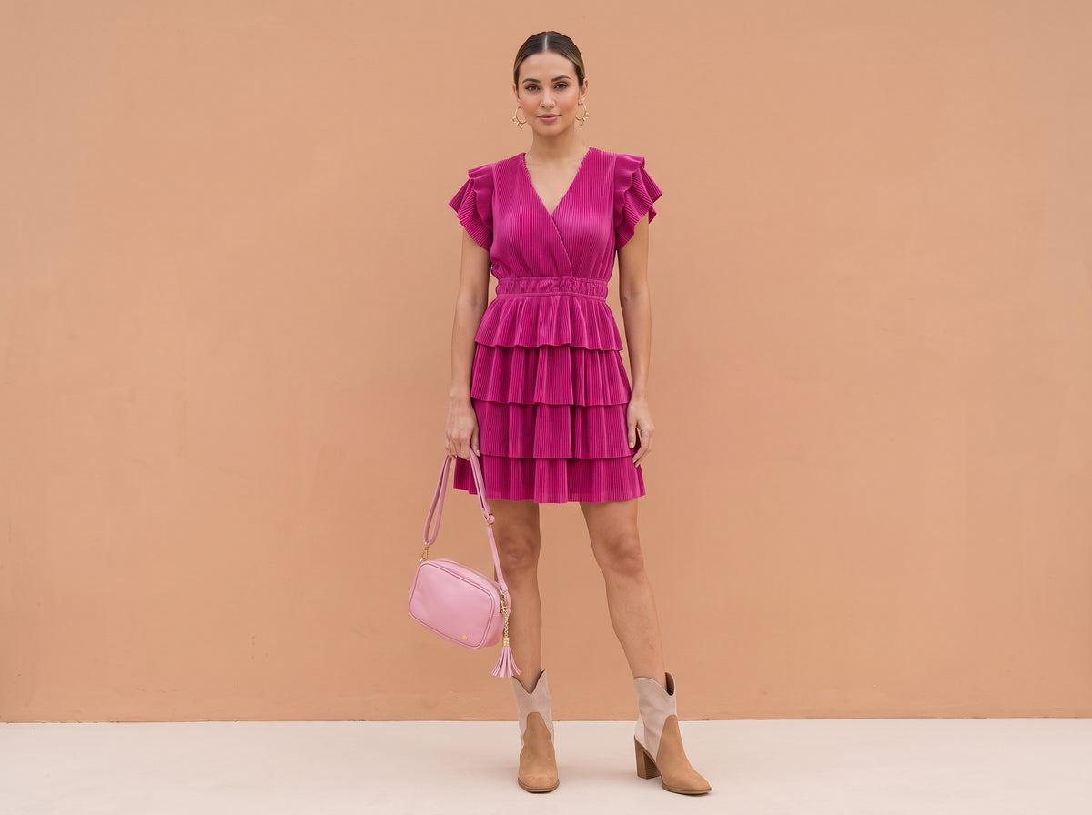 Woman in a pink tiered midi dress with suede ankle boots, a pink tassel handbag and gold bow hoops