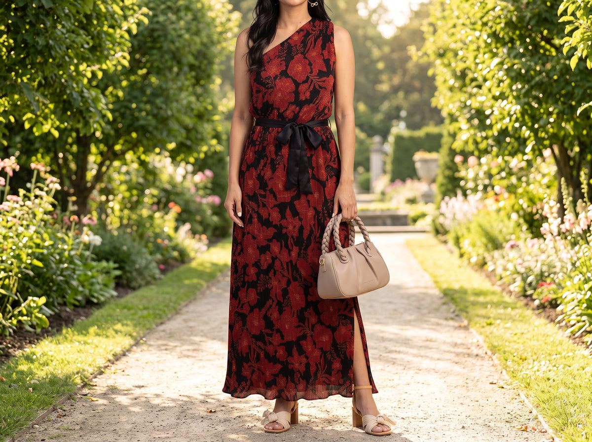 Woman in a red and black floral one-shoulder maxi dress with beige block-heel sandals and a beige braided-handle bag on a garden path