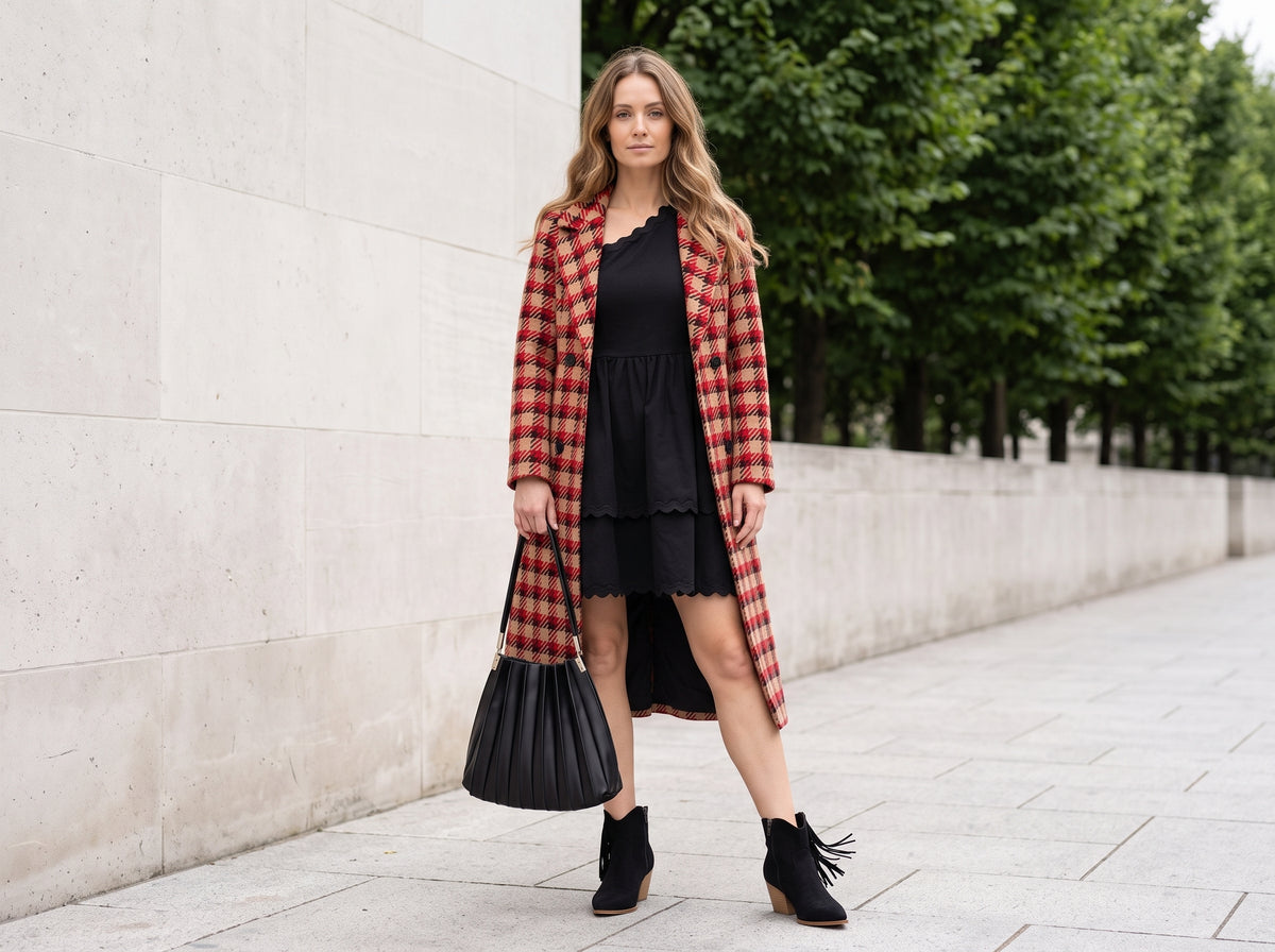 Woman in a red plaid coat over a black one-shoulder mini dress with a black pleated shoulder bag and black tassel ankle boots