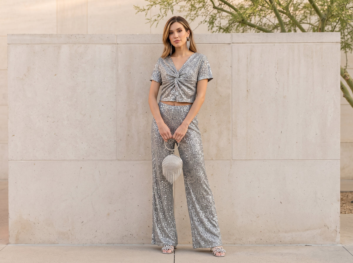 Woman in a silver sequin top and wide-leg pants set with silver sandals, a rhinestone bag and silver earrings