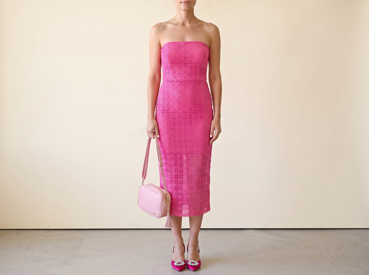 Woman in a strapless pink lace midi dress with pink satin slingbacks, a pink tassel handbag and a gold pearl necklace