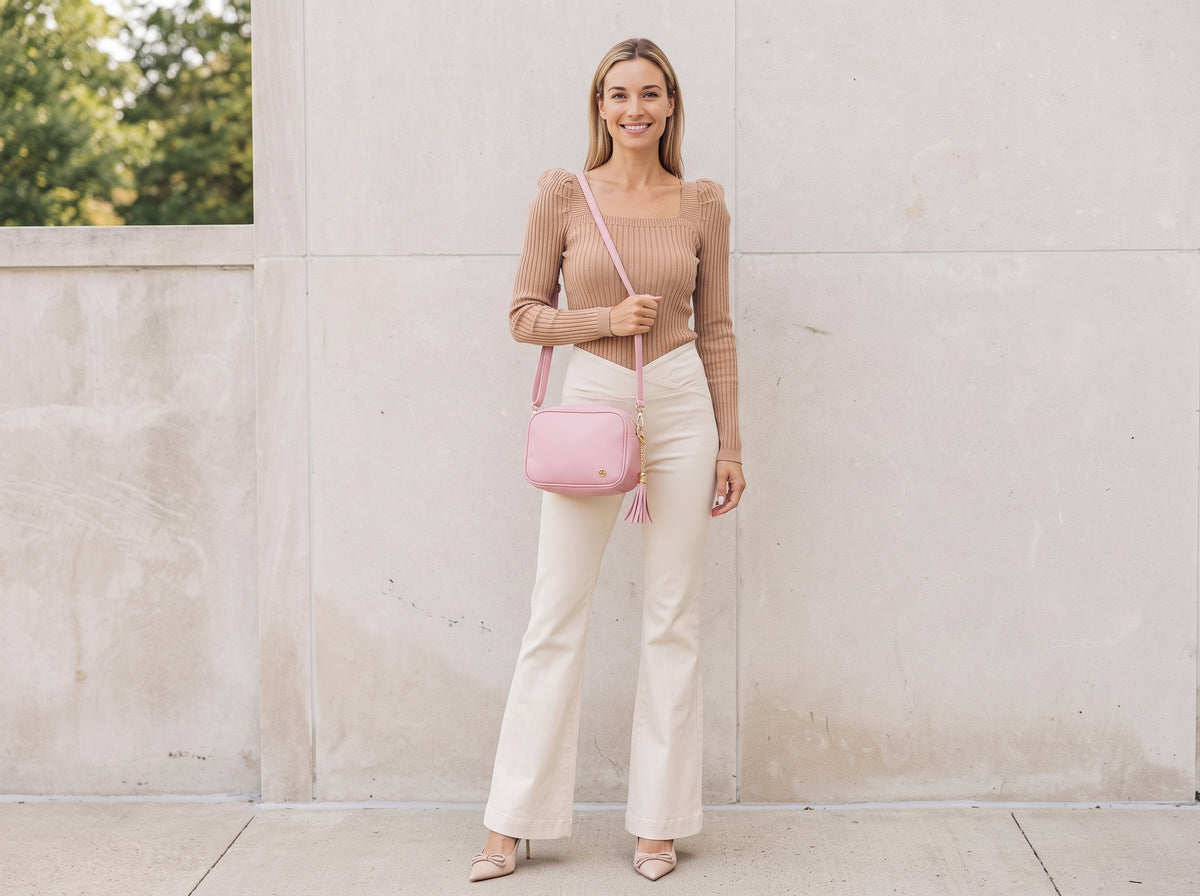 Woman in a tan square-neck sweater and cream flared jeans with a pink crossbody bag and nude pumps