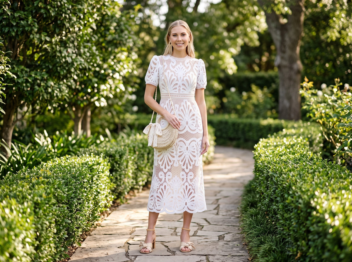 Woman in a white crochet lace midi dress with beige block-heel sandals, a straw crossbody bag and gold fringe earrings