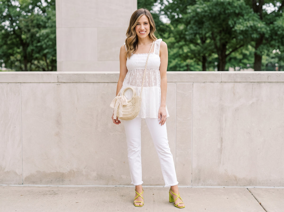 Woman in a white lace smocked top and white cropped jeans with a straw crossbody bag and lime green block-heel sandals