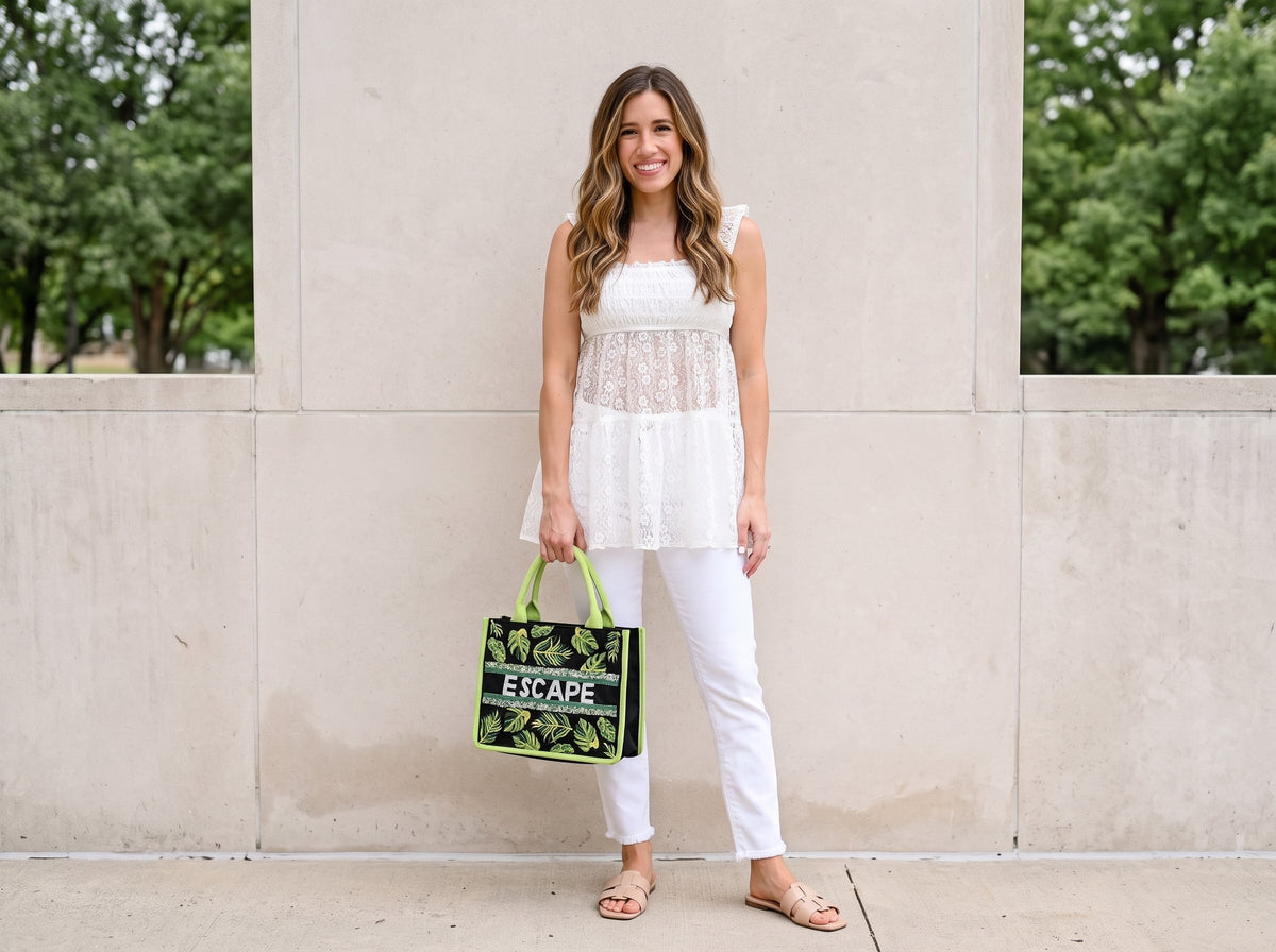Woman in a white lace smocked top and white jeans carrying a green leafy embroidered handbag, with flat slide sandals