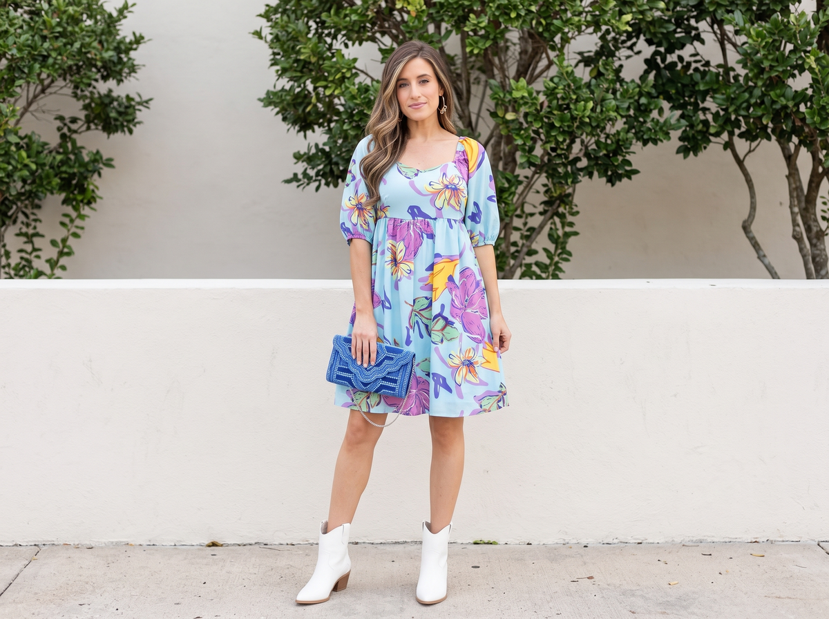 Woman in an aqua floral babydoll dress with white western booties, a blue clutch and gold bow hoop earrings