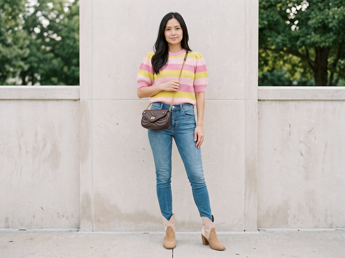 Woman in blue high-rise skinny jeans with a striped sweater, suede booties and a brown quilted crossbody
