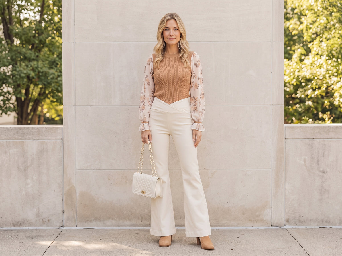 Woman in cream flare jeans with a brown knit sweater, suede booties and a white quilted bag