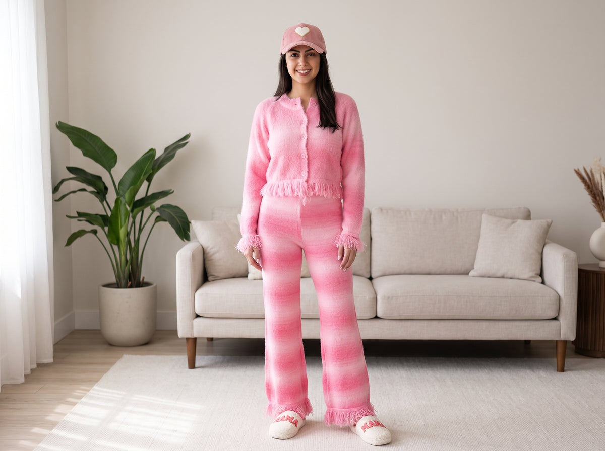 Woman in pink ombre striped lounge pants with a matching fuzzy cardigan, chenille slippers and a pink cap