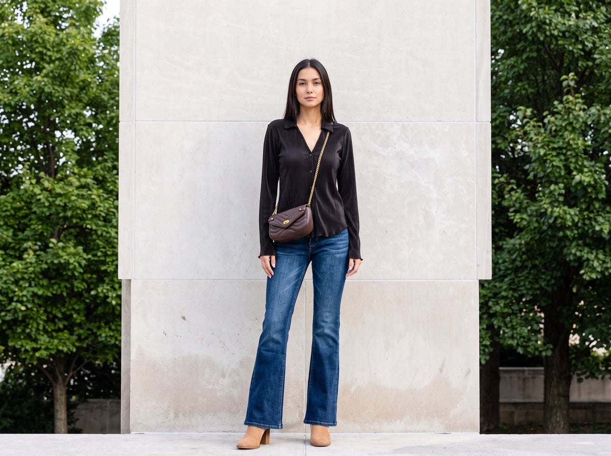 Woman in stone-wash flare jeans with a black pleated top, suede ankle booties and a brown quilted crossbody