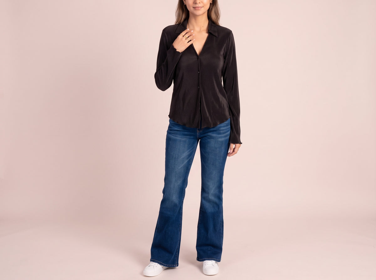 Woman wearing a gold double star ring, a black pleated long-sleeve top, blue flare jeans and white glitter-star sneakers