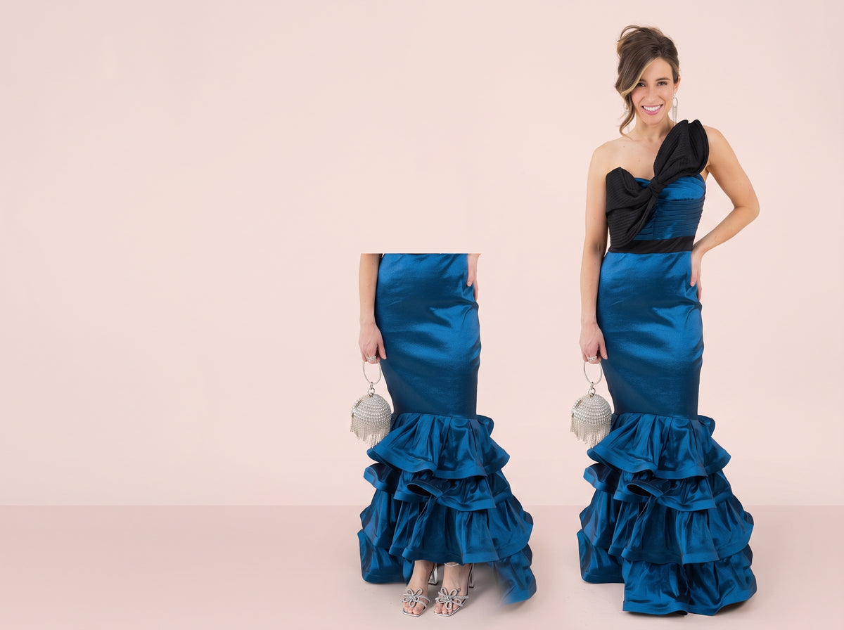 Woman wearing a silver pave X ring, a blue and black ruffled evening gown and holding a round crystal fringe clutch