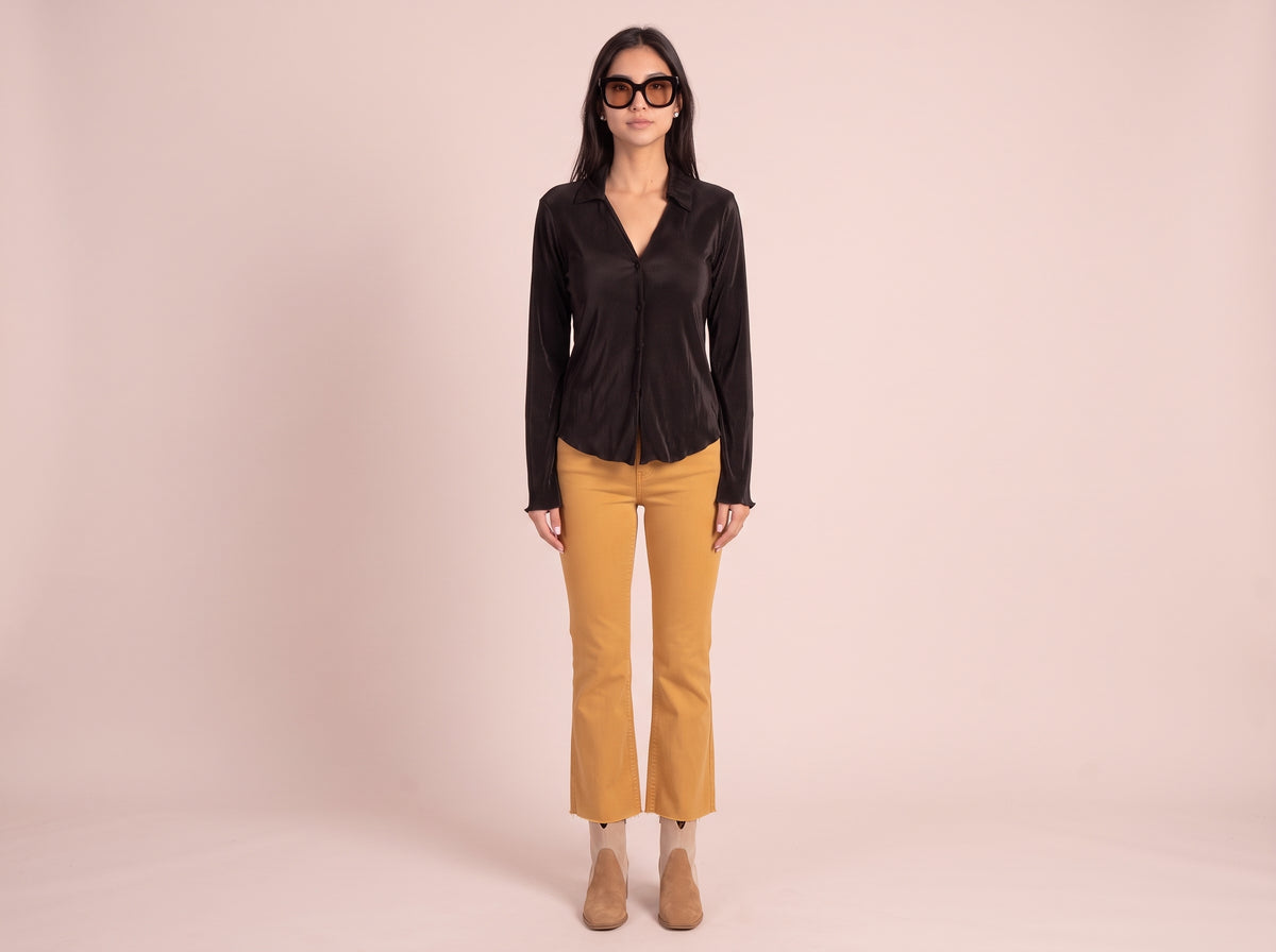 Woman wearing oversized black sunglasses with brown lenses, a black pleated top, mustard kick flare pants and suede ankle booties
