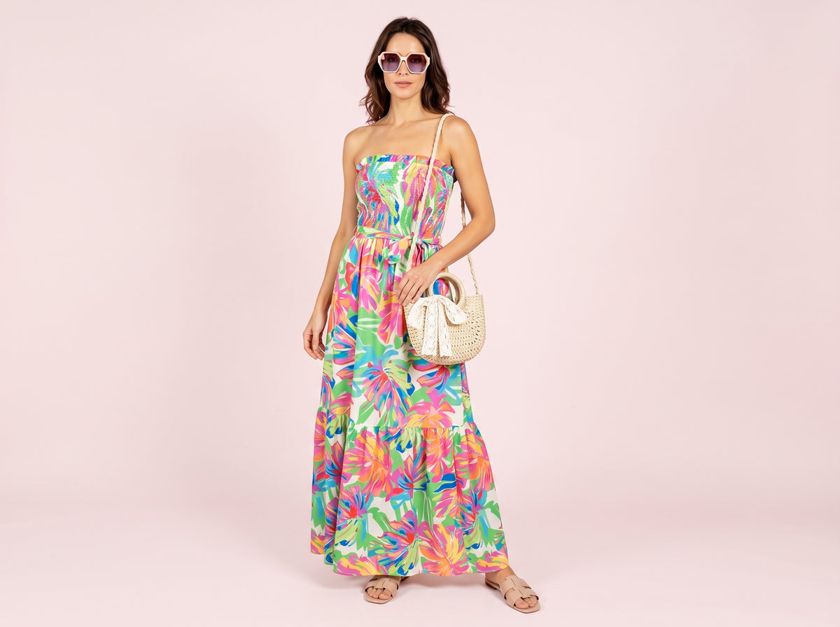 Woman wearing oversized round sunglasses, a strapless print maxi dress, beige flat slide sandals and a round rattan crossbody